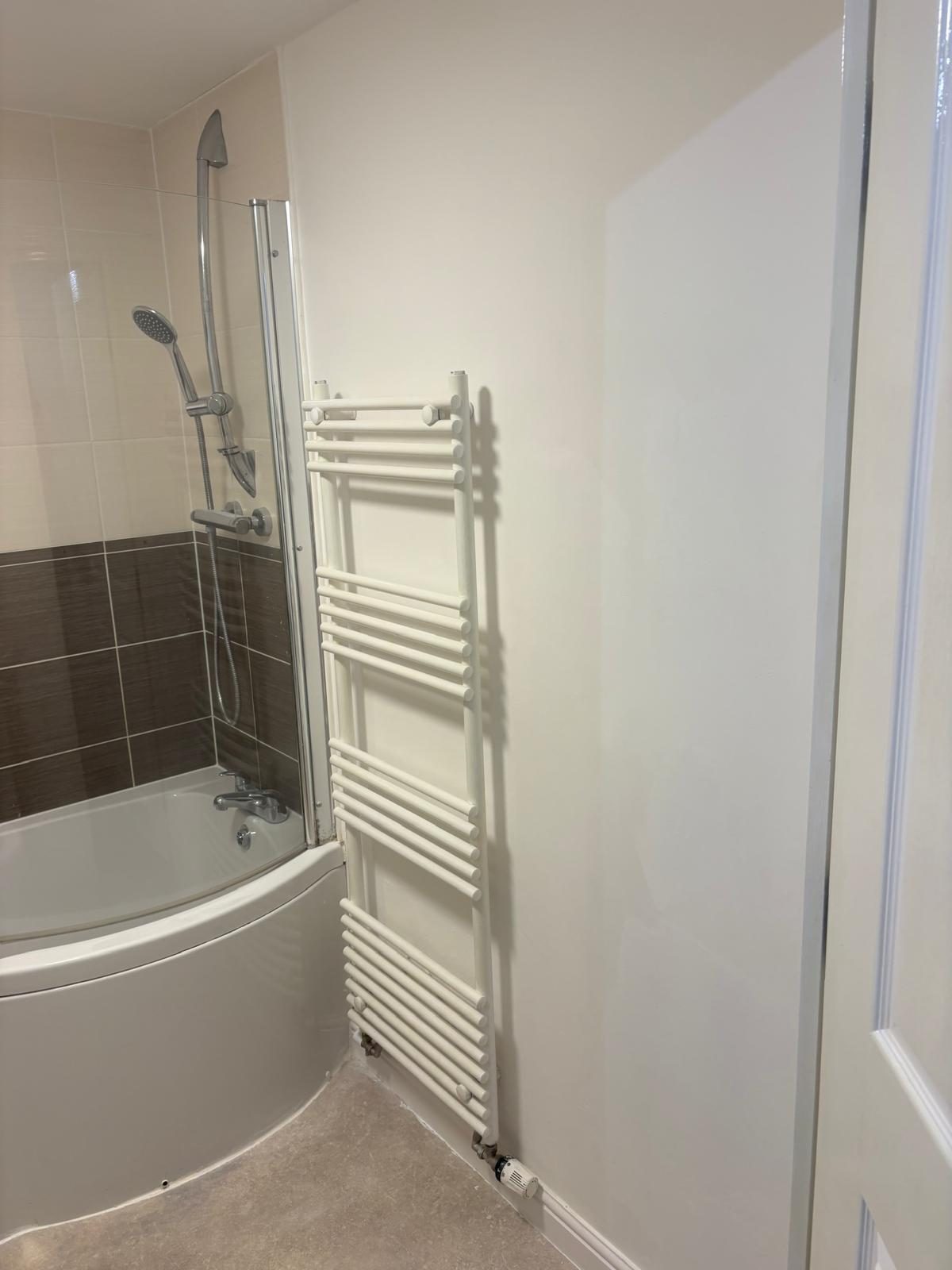 Bathroom of the completed residential flat with bath, shower screen and heated towel rail